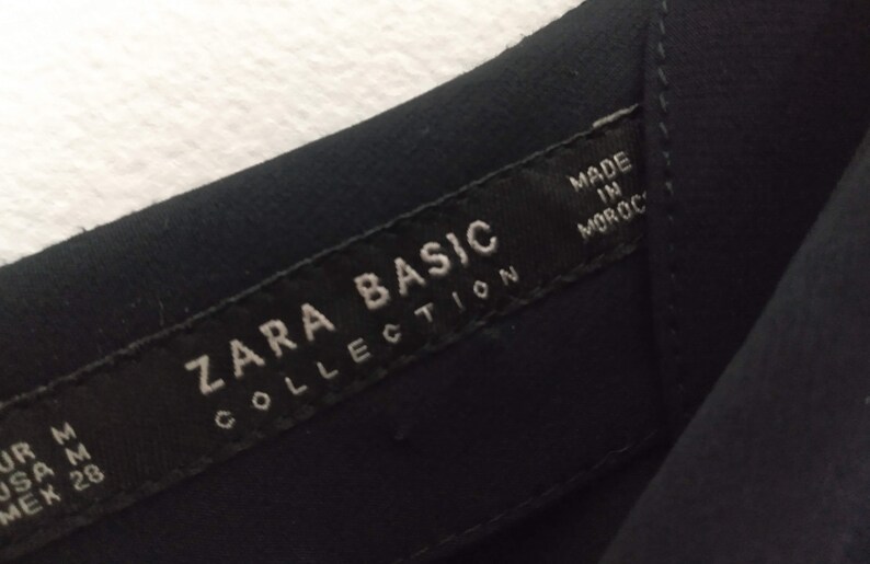 May include: A black Zara Basic Collection tag with white text that reads "Zara Basic Collection" and "Made in Morocco".