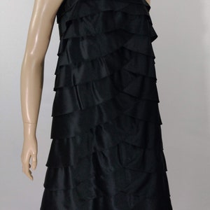 K&ouml;nnte beinhalten: Ein schwarzes tr&auml;gerloses Kleid mit einem mehrstufigen R&uuml;schenrock. Das Kleid ist aus einem glatten, seidenartigen Stoff.
