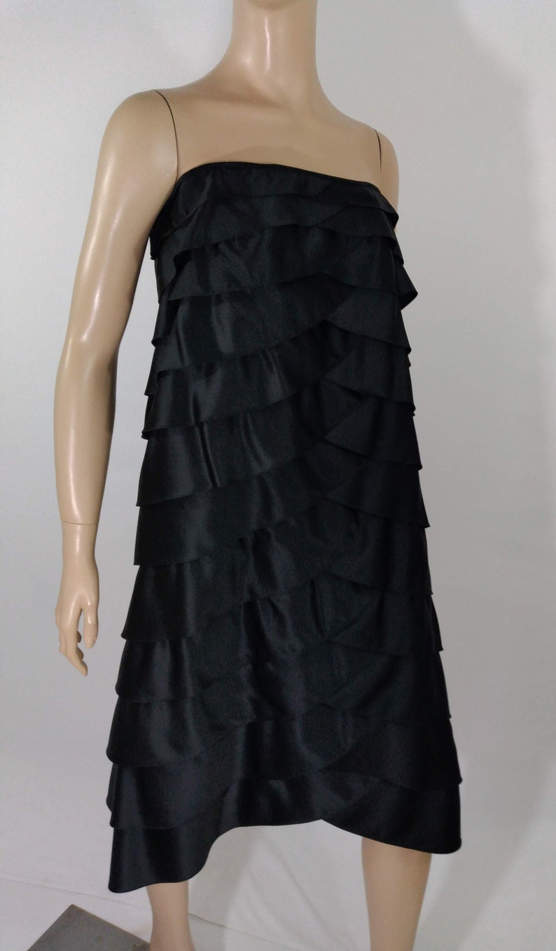 K&ouml;nnte beinhalten: Ein schwarzes tr&auml;gerloses Kleid mit einem mehrstufigen R&uuml;schenrock. Das Kleid ist aus einem glatten, seidenartigen Stoff.