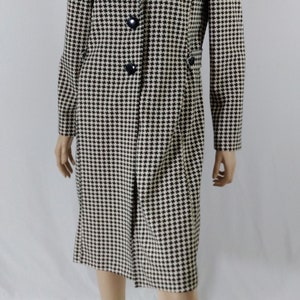 May include: A black and white houndstooth patterned coat with a black collar and buttons. The coat is knee-length and has a fitted silhouette.