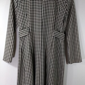 May include: Black and white houndstooth patterned coat with long sleeves and a collar.