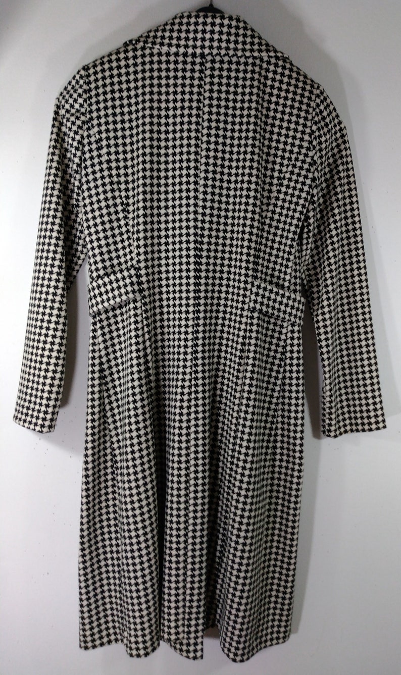 May include: Black and white houndstooth patterned coat with long sleeves and a collar.