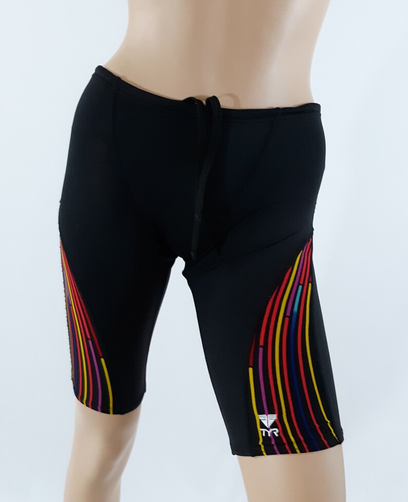 May include: Black swim shorts with a colorful stripe design on the sides. The shorts have a drawstring waistband and the TYR logo is on the right leg.