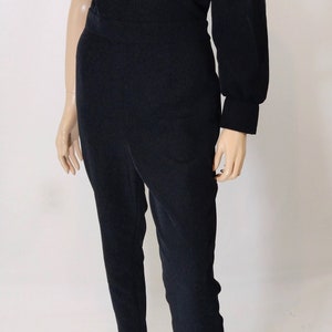 May include: A black one-shoulder jumpsuit with a long, puffy sleeve. The jumpsuit has a fitted bodice and straight legs.