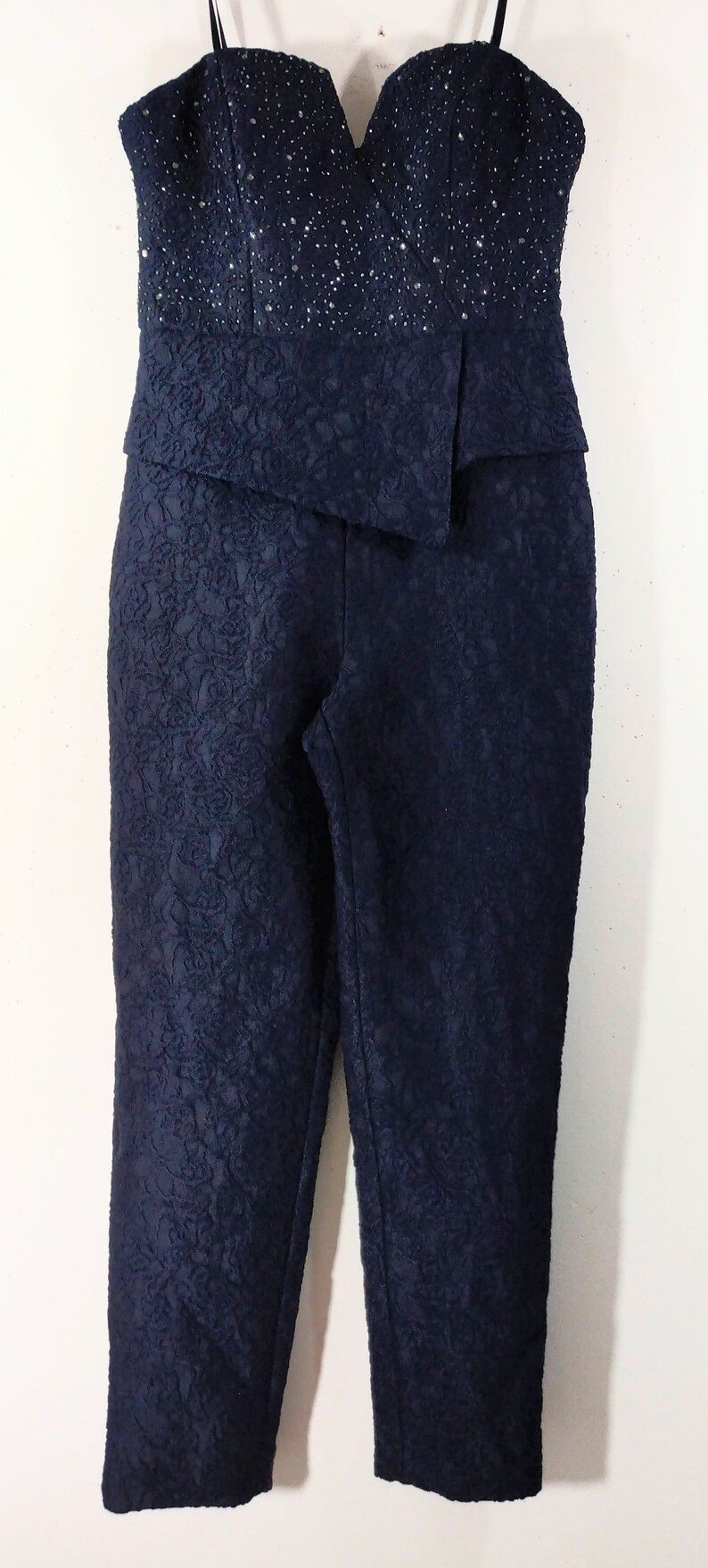 May include: A navy blue jumpsuit with a strapless bodice and a floral pattern. The bodice is embellished with rhinestones.
