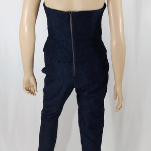 May include: A black strapless jumpsuit with a zipper down the back. The jumpsuit has a textured fabric and a cropped leg.