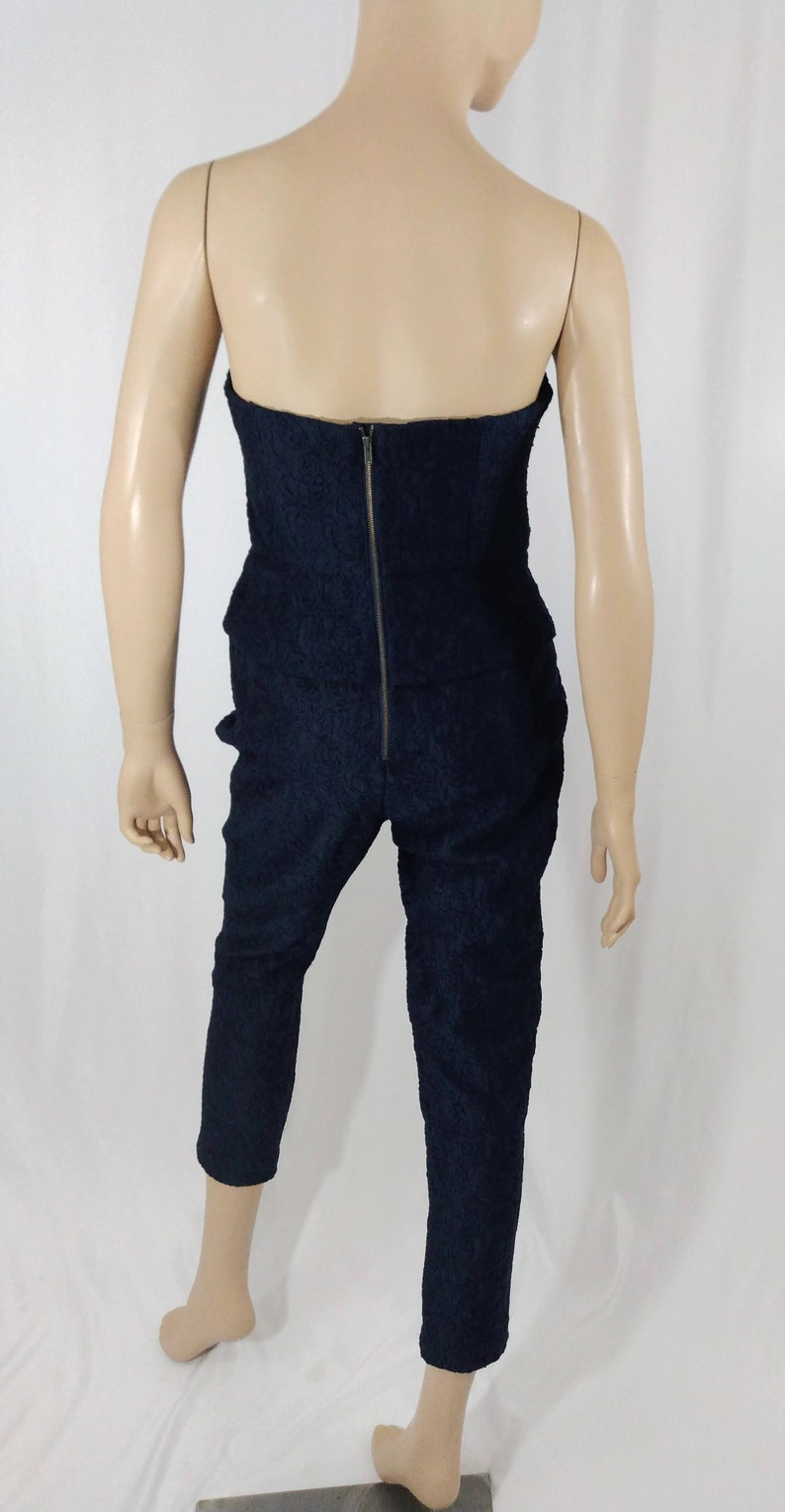May include: A black strapless jumpsuit with a zipper down the back. The jumpsuit has a textured fabric and a cropped leg.