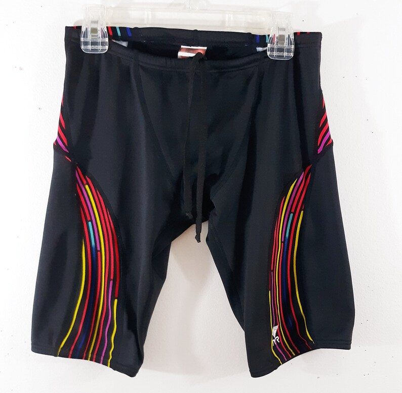 May include: Black swim trunks with a colorful geometric pattern on the sides. The trunks have a drawstring waist.
