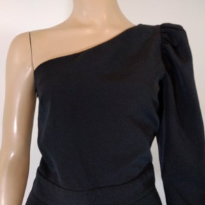 May include: A black one-shoulder dress with a long sleeve on one side and a short sleeve on the other. The dress has a fitted bodice and a flowing skirt.