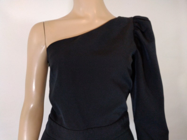 May include: A black one-shoulder dress with a long sleeve on one side and a short sleeve on the other. The dress has a fitted bodice and a flowing skirt.