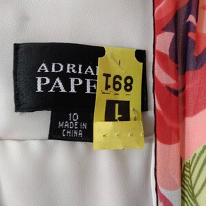 Puede incluir: Un vestido blanco con estampado floral. El vestido tiene una etiqueta negra que dice "Adrianna Papell" y una etiqueta amarilla que dice "T68". El vestido es talla 10 y hecho en China.