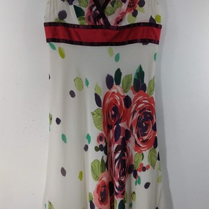 Puede incluir: Un vestido blanco sin mangas con estampado floral rojo y morado. El vestido tiene un escote en V y una cinta roja alrededor de la cintura.
