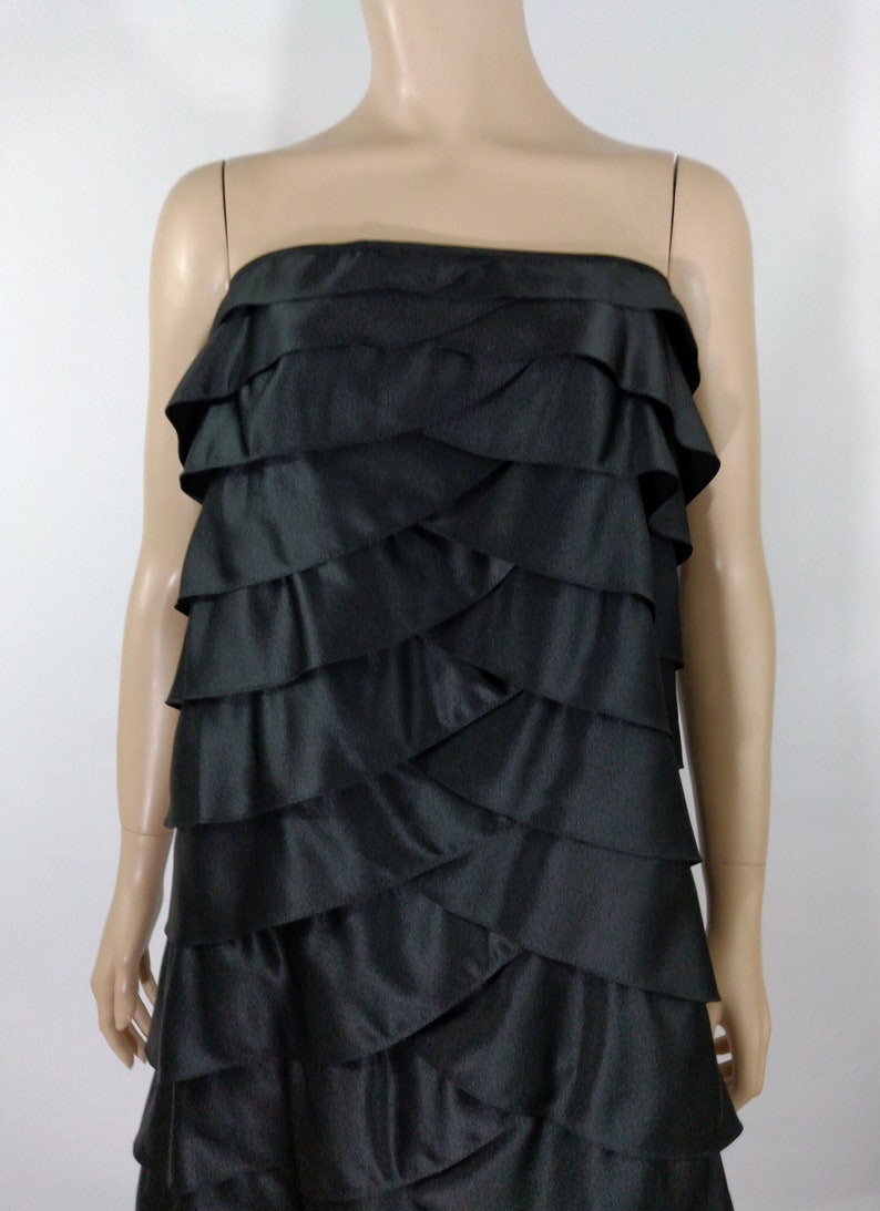 K&ouml;nnte beinhalten: Ein schwarzes tr&auml;gerloses Kleid mit mehreren R&uuml;schenlagen. Das Kleid ist aus einem glatten, seidenartigen Stoff.