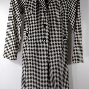 May include: Black and white houndstooth long coat with a button closure and a collar. The coat has a label that reads "JULIETTE TAYLOR".