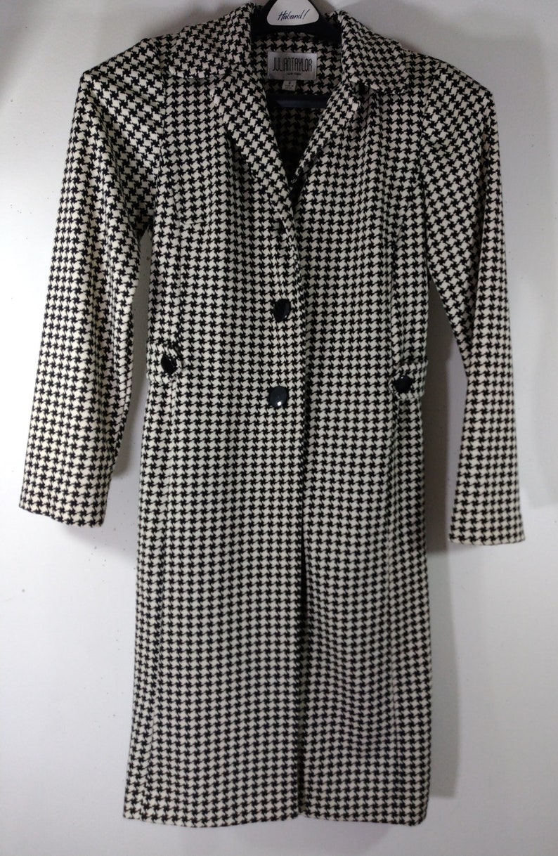 May include: Black and white houndstooth long coat with a button closure and a collar. The coat has a label that reads "JULIETTE TAYLOR".