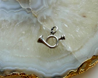May include: A silver charm in the shape of a French horn. The charm is on a white and gold agate background.