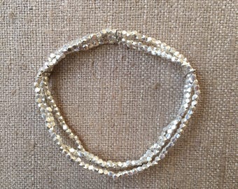 Könnte beinhalten: Ein silbernes Armband aus kleinen, facettierten Perlen. Das Armband ist geschichtet und scheint flexibel zu sein.