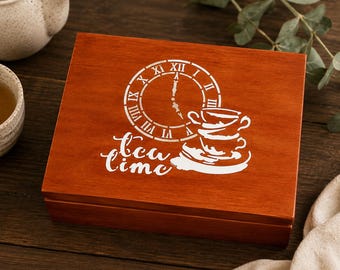 May include: A rectangular wooden box with a warm brown finish featuring a white graphic on the lid. The design includes a clock face with Roman numerals, a stack of two teacups, and the script text "tea time" printed below the clock.