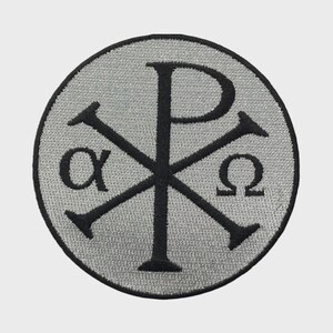 Può includere: Una toppa ricamata circolare con sfondo grigio argento e bordo nero. Il design presenta un simbolo Chi-Rho nero al centro, affiancato dalle lettere greche alfa a sinistra e omega a destra, realizzate con filo di colore nero.