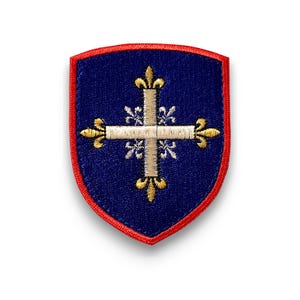 Puede incluir: Parche en forma de escudo con fondo azul marino y borde rojo. El parche presenta una cruz dorada con detalles de flor de lis. La cruz está centrada en el parche.