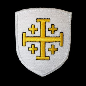Könnte beinhalten: Weißer Stoff-Patch in Form eines Schildes mit einem goldenen gestickten Kreuz mit vier kleineren Kreuzen darum herum.