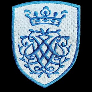 Può includere: Toppa ricamata a forma di scudo, con una corona azzurra e un monogramma intrecciato su sfondo bianco. La toppa ha un bordo azzurro ed è posta su uno sfondo nero.