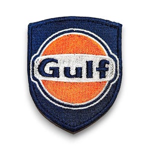 May include: A blue and orange embroidered patch with the word "Gulf" in white lettering. The patch is shaped like a shield.