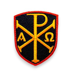 Op de afbeelding: Een geborduurde zwarte en rode patch met een geel kruis en de letters "P", "A" en "Ω" in het midden.