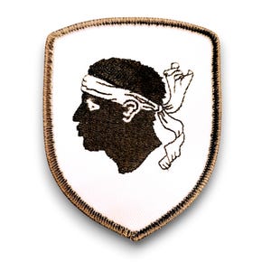 Può includere: Una toppa bianca con un contorno ricamato marrone a forma di scudo. Lo scudo presenta una silhouette in bianco e nero di una testa umana con una fascia.