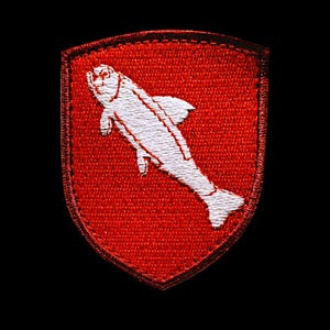 Puede incluir: Un parche bordado rojo en forma de escudo con un diseño de pez blanco.