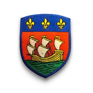 Könnte beinhalten: Ein blauer und orangefarbener gestickter Aufnäher mit einem Schiff und drei Lilien.