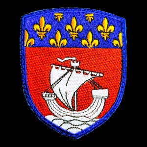 Peut inclure: Un écusson brodé bleu et rouge avec un navire blanc et des fleurs de lys jaunes. Le navire navigue sur une vague blanche.