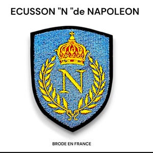 Può includere: Una toppa ricamata blu con una corona dorata, la lettera N e una ghirlanda di foglie. La toppa ha la forma di uno scudo e ha un bordo nero. Il testo "BRODE EN FRANCE" è sotto la toppa.
