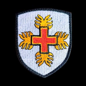 Può includere: Toppa ricamata bianca con una croce rossa circondata da quattro disegni gialli a forma di fiamma. La toppa ha la forma di uno scudo.