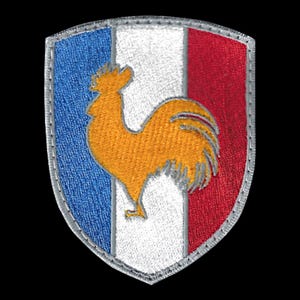 Peut inclure: Un écusson brodé bleu, blanc et rouge avec un coq doré au centre. L'écusson est en forme de bouclier et a une bordure grise.