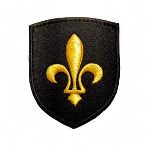 Peut inclure: Un écusson brodé noir en forme de bouclier avec un motif de fleur de lys dorée.