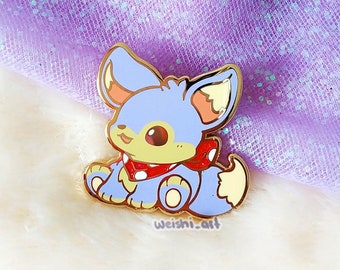 May include: A gold-colored enamel pin featuring a cartoon fox with blue fur, a red and white scarf, and a yellow tail. The pin is on a white background.