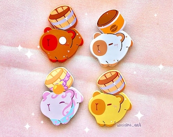 May include: A collection of colorful, cartoon-style bear pins. Each pin features a bear with a barrel on top. The bears are in shades of brown, white, pink, and yellow, with various details. The background is a soft pink.