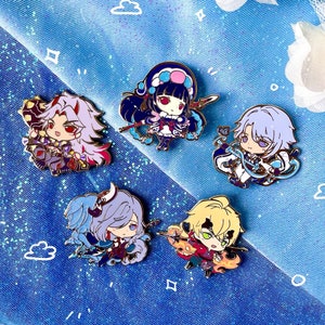 Puede incluir: Cinco pines de esmalte con personajes de anime. Los pines son coloridos y presentan diferentes personajes con diseños únicos. Los pines están sobre un fondo azul y blanco brillante.