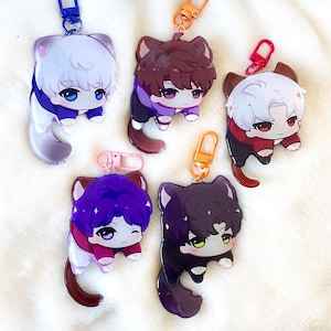 May include: Five colorful cat-themed keychains with different colored hair and clothing. Each keychain has a white cat face with black eyes and a small pink nose. The keychains are made of clear acrylic and have a silver metal ring.