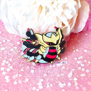 Könnte beinhalten: Eine goldene, schwarze und rote Emaille-Anstecknadel mit einer Cartoon-Darstellung des Pokémon "Mega Rayquaza".