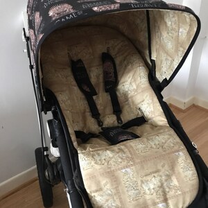 May include: A black stroller with a Game of Thrones themed canopy and seat liner. The canopy is black with a white Game of Thrones logo and the seat liner is beige with a map of Westeros.