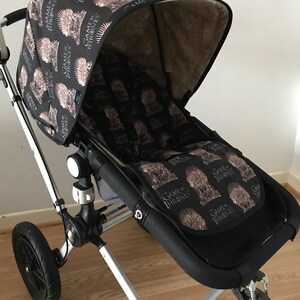 May include: A black stroller with a Game of Thrones themed canopy and seat liner. The canopy is black with a repeating pattern of the House Stark sigil, a direwolf head with a crown of thorns. The seat liner is black with a repeating pattern of the Iron Throne.