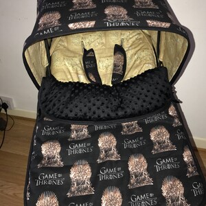 May include: A black stroller canopy and liner with a repeating pattern of the Iron Throne from the TV show Game of Thrones. The canopy is folded down and the liner is in the stroller.