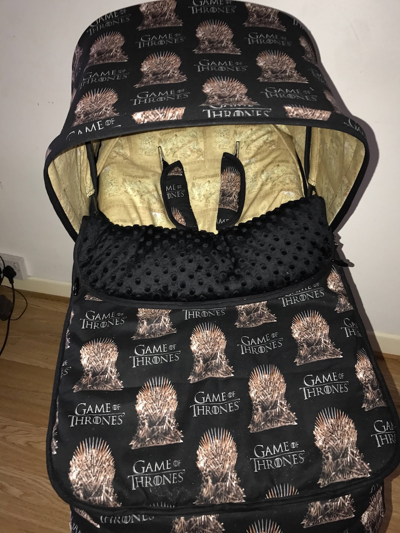 May include: A black stroller canopy and liner with a repeating pattern of the Iron Throne from the TV show Game of Thrones. The canopy is folded down and the liner is in the stroller.
