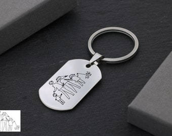 Könnte beinhalten: Silberner Schlüsselanhänger mit einem Hund und einer Familie aus fünf Strichmännchen, die auf ein rechteckiges Schild graviert sind. Der Schlüsselanhänger liegt auf einer grauen Oberfläche.