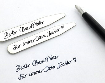 Op de afbeelding: Twee zilverkleurige kraagstijvers met zwarte handgeschreven tekst: "Bester (Braut) Vater" en "Für immer Deine Tochter". Een zwarte pen ligt op een wit oppervlak. Extra tekst is hieronder zichtbaar.
