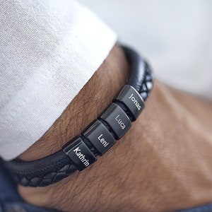 May include: Black leather bracelet with four silver metal name tags. The names on the tags are Kathrin, Leni, Luca, and Jonas.