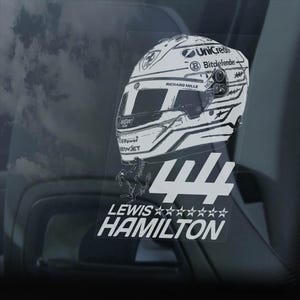 May include: A white and grey racing helmet with the number 44 and the name Lewis Hamilton printed below. The helmet has sponsors' logos including UniCredit and Bitdefender.