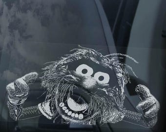 May include: A black and white graphic of a Muppet character with a wide grin and outstretched arms, applied to a car window. The image is next to a red and black car tail light.